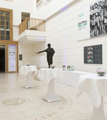 Large white room with high ceilings and tall white tables in front of a bronze statue
