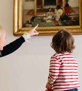 A woman crouched down beside a small child and pointing at a painting on a tour of the National Gallery of Ireland.