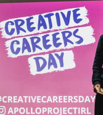 Two people stand on stage in front of a bright pink screen with the words Creative Careers Day written across it.