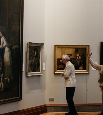 Photo of two women and a man looking at oil paintings in a gallery.