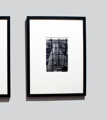 Two black and white photographs, framed and mounted, hanging side by side on a grey wall.