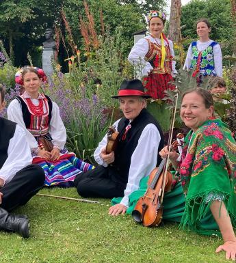 A group of musicians in colourful clothing sit in a park