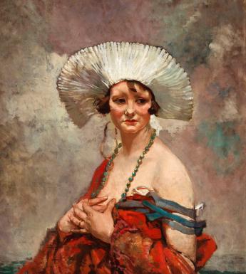 A woman sits wearing a starched white headdress and long beaded necklace. A shawl has fallen off her bare shoulders. 