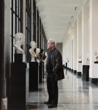 Writer John Banville stands in a corridor of the Prado Museum looking at a row of busts.