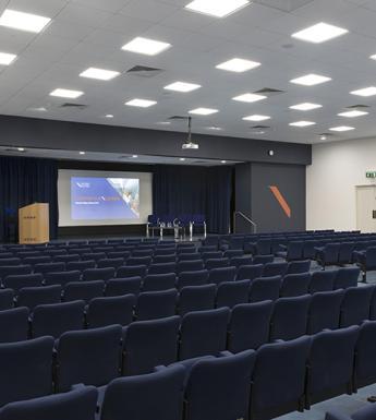 Lecture theatre with rows of dark blue chairs facing a screen
