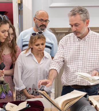 A group of people are gathered around looking at a rare book on display