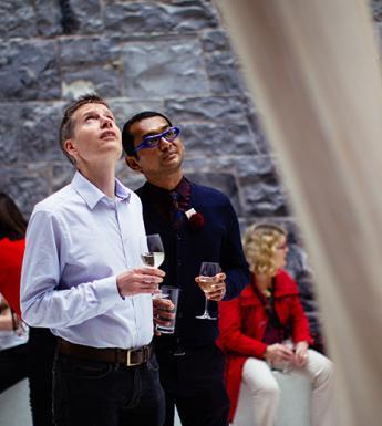 Photography of two men holding glasses of wine while looking a sculpture in a gallery.