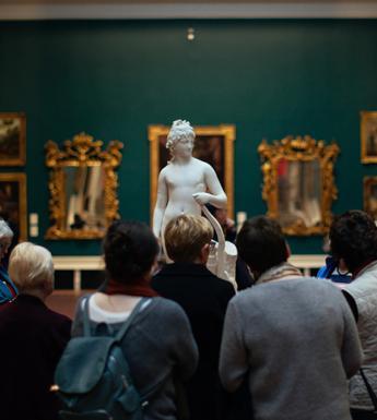 Photo of a group of people looking at a marble statue in a gallery room painted green and hung with gilt-framed paintings.
