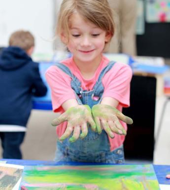 Photo of girl holding her hands, covered in green chalk, out for the camera.