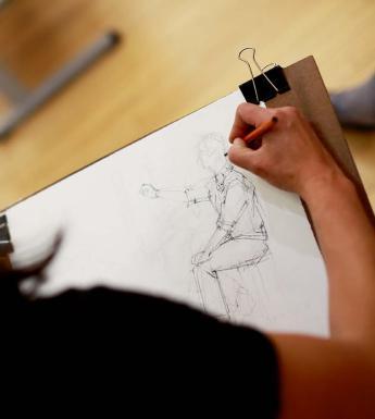 Photo of a woman drawing a human figure on paper.