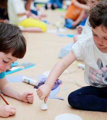 Photo of two children drawing on a giant sheet of brown paper on the floor.