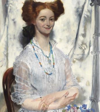 A woman with vibrart red hair in an updo smiles at the viewer. She wears a white dress and has flowers on her lap. Around her neck she has beaded necklaces, and has rings on her fingers. 