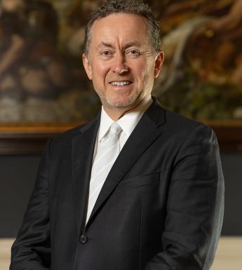 A man in a suit with a white tie in front of a painting