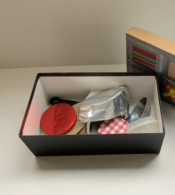 A shoe box filled with household objects, with textured materials taped to the lid