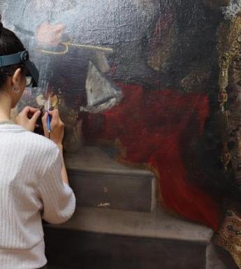 A woman wearing a magnifying visor working on an oil painting in a conservation studio