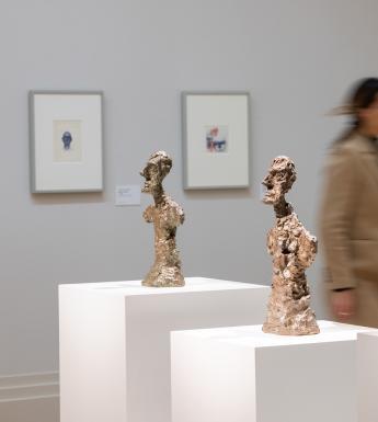 Woman walking past three sculptures in the exhibition Giacometti: From Life