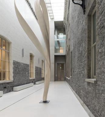 Large room with stone walls, a glass ceiling and a large spiral sculpture.