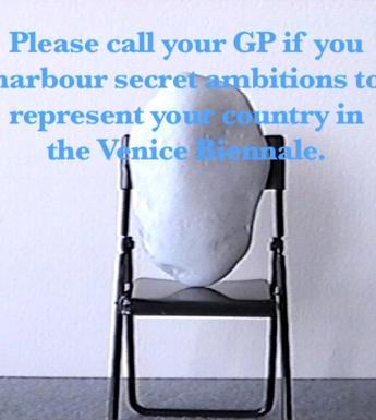A still from a film showing a stone on a folding chair. Blue text overlaid on the image says "Please call your GP if you harbour secret ambitions to represent your country in the Venice Biennale".
