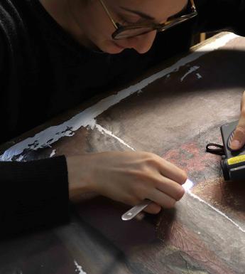 A conservator working on an oil painting