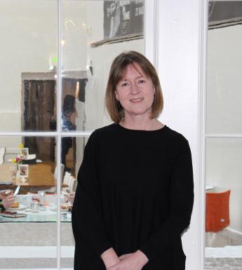A female figure with a brown bob and a black dress stands in front of a large window