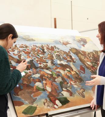 Two women look closely at a painting in a conservation studio