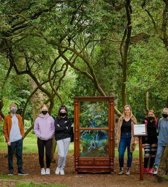 Group of masked young people pose among trees beside a sculpture