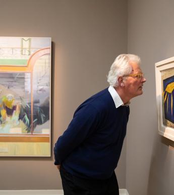 Sean Rainbird looking at a semi-abstract blue and yellow painting of crayfish by Anne Yeats.