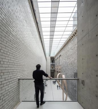 Photography of a male figure looking over a balcony railing to a grand internal courtyard made of grey stone.