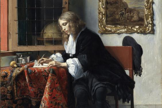 Detail of a man writing at a desk covered in a heavily patterned cloth.