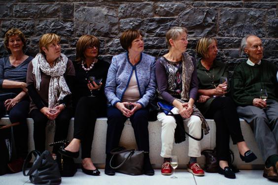 Photo of six women and a man seated in a row on a bench against a stone wall.