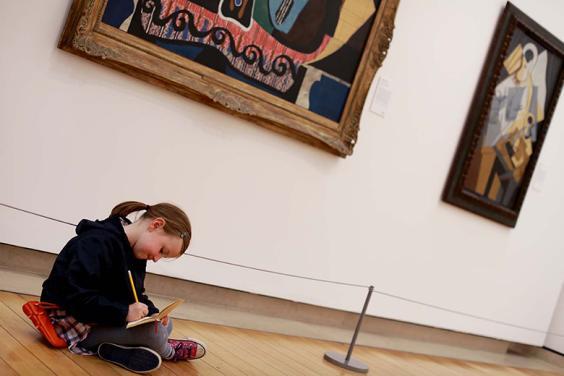 Photo of a young girl sitting on the floor in a gallery and drawing.