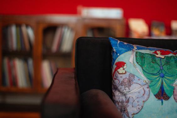 Photo of the corner of a sofa with a cushion decorated with a painting by Harry Clarke. A book case is out of focus in the background.