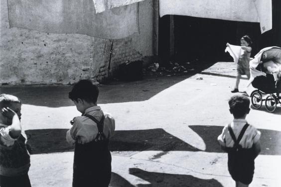 Black and white photograph of children playing in a yard beneath a clothes line of washing.