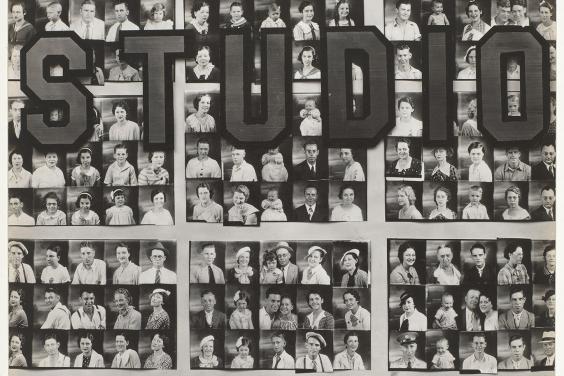 Black and white photo of a photography studio window filled with passport-size photos of people. The word studio is written on the window.