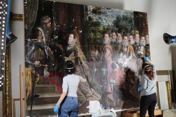 Two conservators applying isolating layer of varnish to a large oil painting