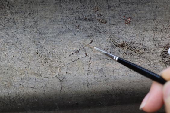 A close up shot of a hand holding a small brush and working on retouching old losses and damages on the canvas.