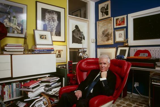 Photo of Alexander Walker in his apartment sitting in a red leather armchair with lots of art hanging on the walls