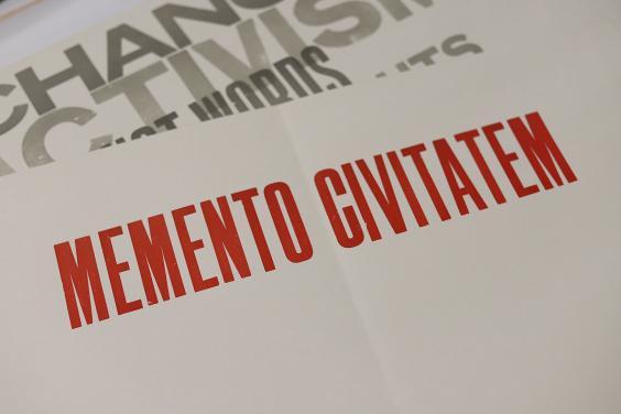 A sheet of paper with memento civitatem printed in red block capitals, with another sheet of paper visible beneath with fragments of words including activism and change