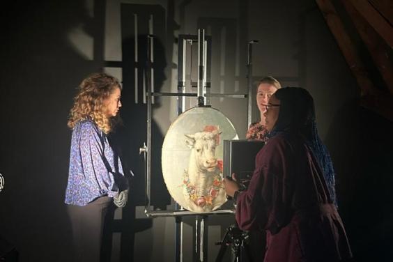 A small oval painting of a bull stands on an easel in a darkened studio. People stand around it, scanning and photographing it