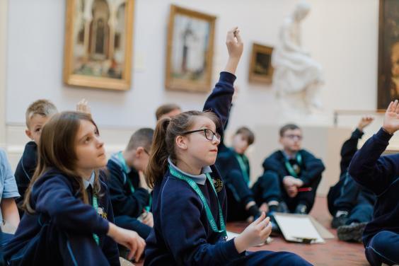 A group of young children in school uniform sit on the floor of an art gallery.