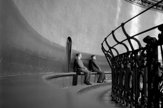 Black and white photograph of two men sitting on a bench within the curved dome of St Paul's Cathedral