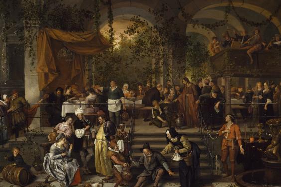 A banquet scene filled with figures. The table is set up beside large arches through which we can see trees and greenery.