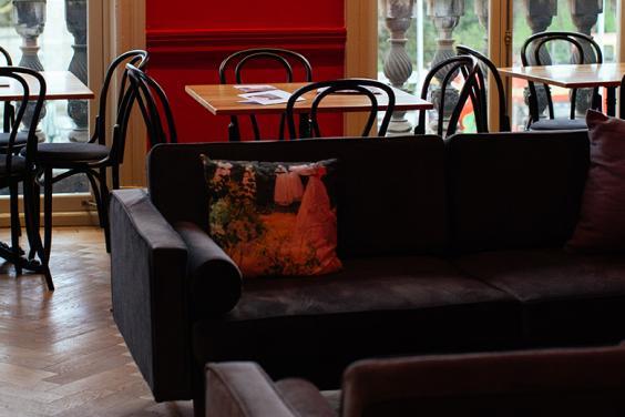 Photograph of an interior with red walls, grey couches and dining tables and chairs with large windows looking out on trees.