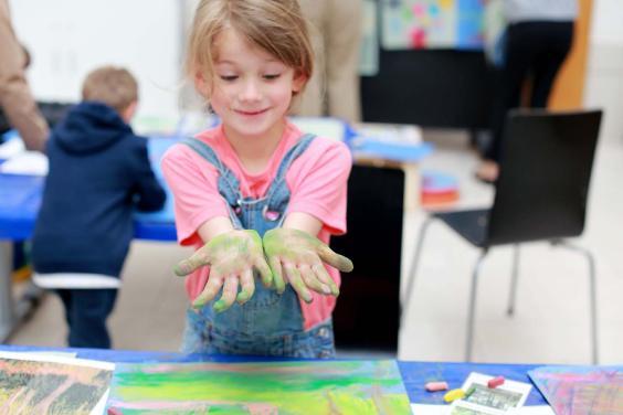 Photo of girl holding her hands, covered in green chalk, out for the camera.