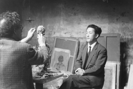 Photograph of Giacometti in his studio make a portrait bust of Yanaihara who is sitting and posing in a chair
