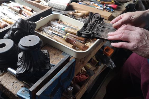 Photo of hands reaching towards woodcarver's tools laid out on a bench
