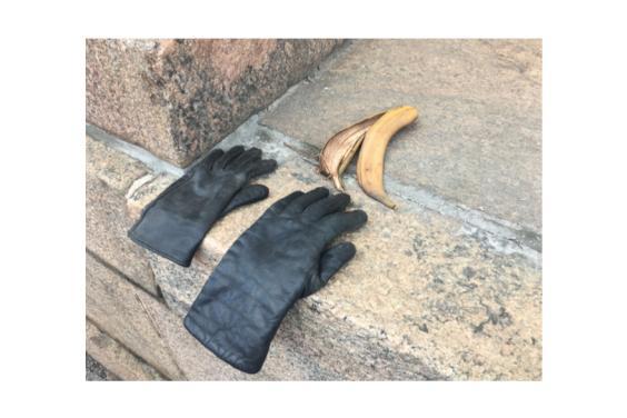 Photo of two black gloves lying on a brick wall next to a banana peel.