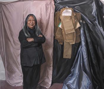 Painted full-length portrait of designer John Rocha wearing all black and standing in front of a wall covered in sheets of fabric and paper patterns.