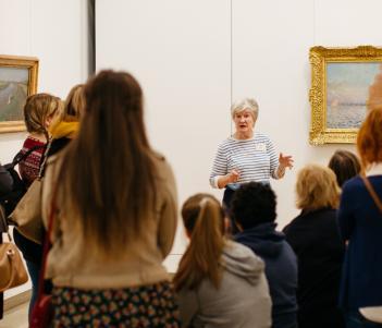 Tour guide speaking to a group in front of a painting by Monet