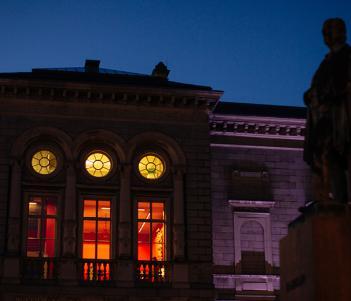 Nighttime photo of the exterior of the Merrion Square entrance to the National Gallery of Ireland with the windows illuminated and an outdoor sculpture silhouetted against the sky.